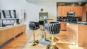 Cocina moderna con armarios de madera, microondas integrado y comedor con una mesa redonda y dos taburetes de bar.