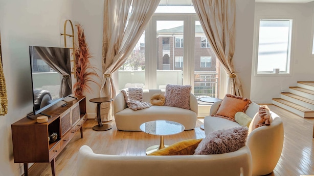 Una sala de estar moderna con un sofá, sillones, una mesa de centro y un televisor sobre un mueble de madera.