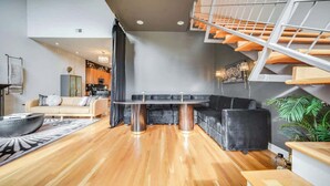 Una sala de estar moderna con piso de madera, un sofá negro, una mesa redonda y una escalera con barandales naranja.
