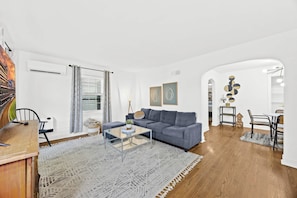 A modern living room with a grey sofa, a glass coffee table, and a dining area with a table and chairs.