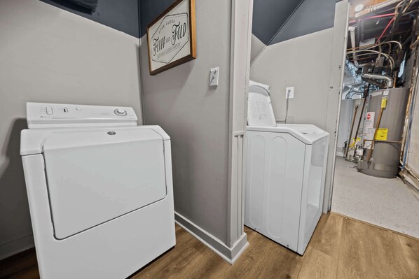 A laundry room with two white washing machines, a wooden floor, and exposed ductwork.