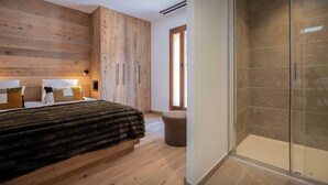 A bedroom with a wooden headboard, a bed with a dark blanket, a bedside table with a lamp, and a glass shower enclosure.