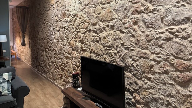 Una sala moderna con una pared de piedra, un televisor de pantalla plana, un banco de madera y una pequeña mesa con un objeto decorativo.