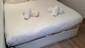 Una cama bien hecha con sábanas blancas y dos toallas enrolladas sobre ella.