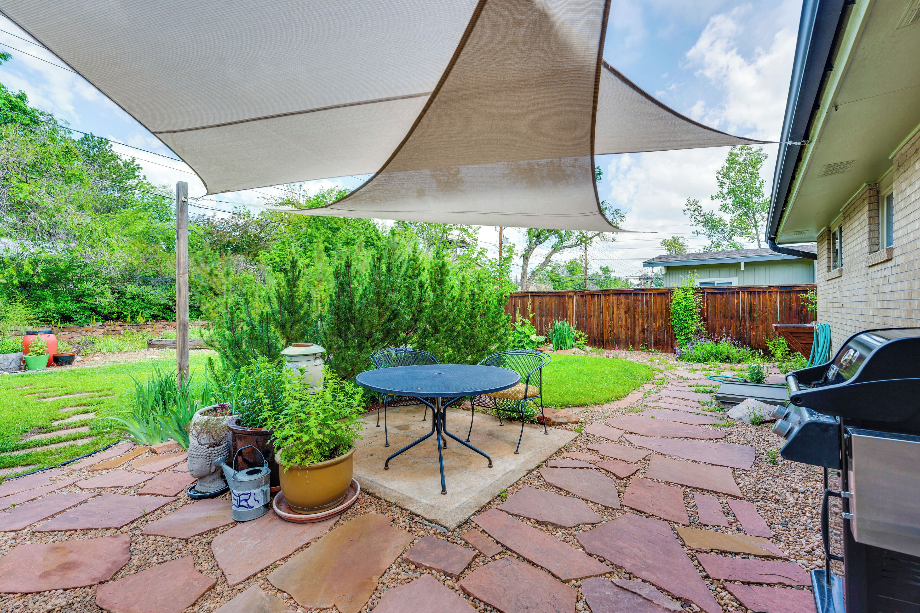 En terrasse med et bord, stole, grill og en stor parasol der giver skygge.