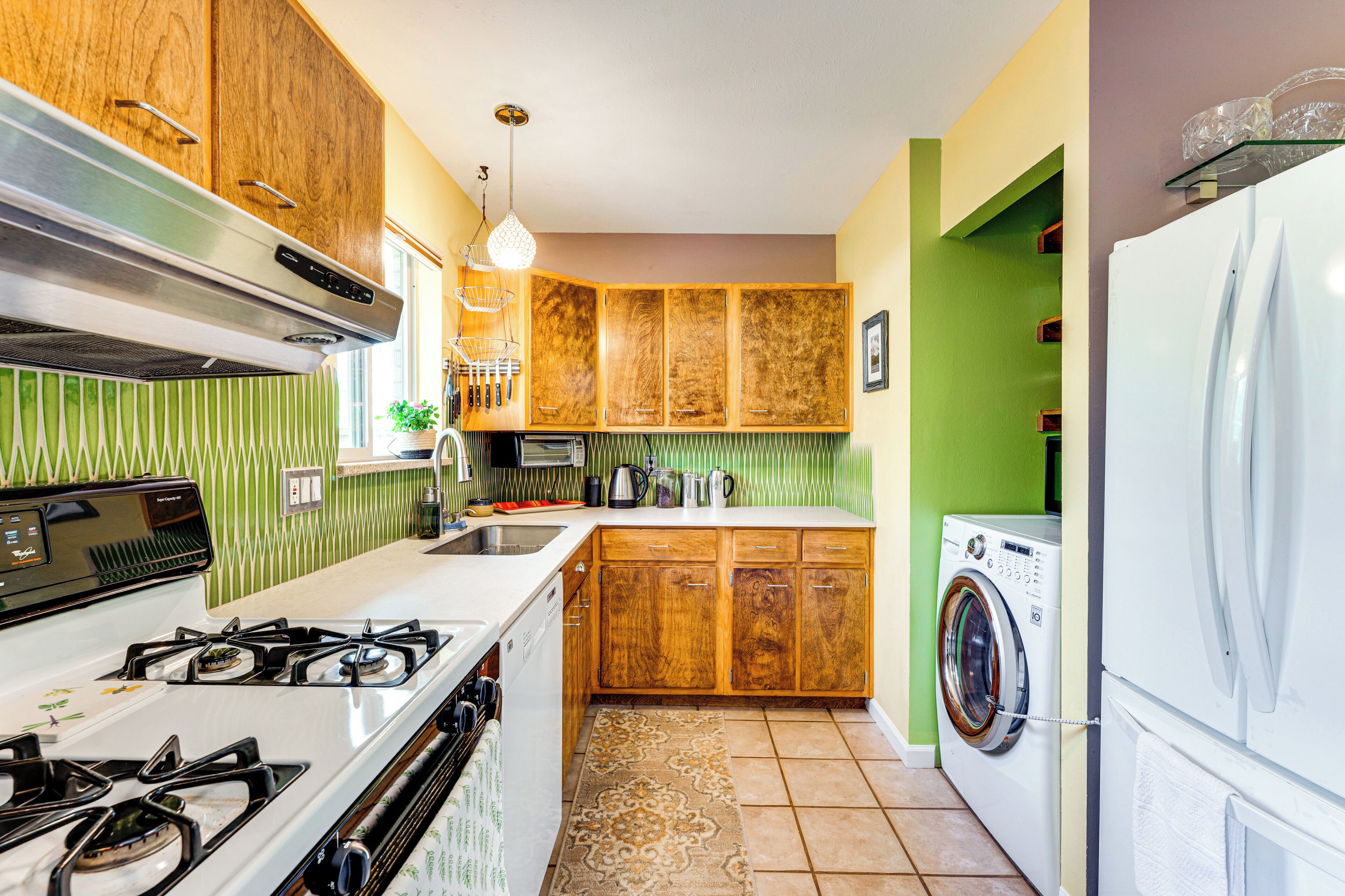 A compact kitchen with wooden cabinets, a gas stove, a washing machine, and a refrigerator.
