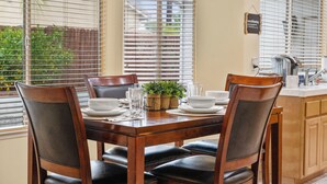 A dining area with a wooden table set for four, surrounded by chairs, with a window and blinds in the background. - Explore Ramona's Vineyards: Tranquil Home w/ Yard (Ramona)