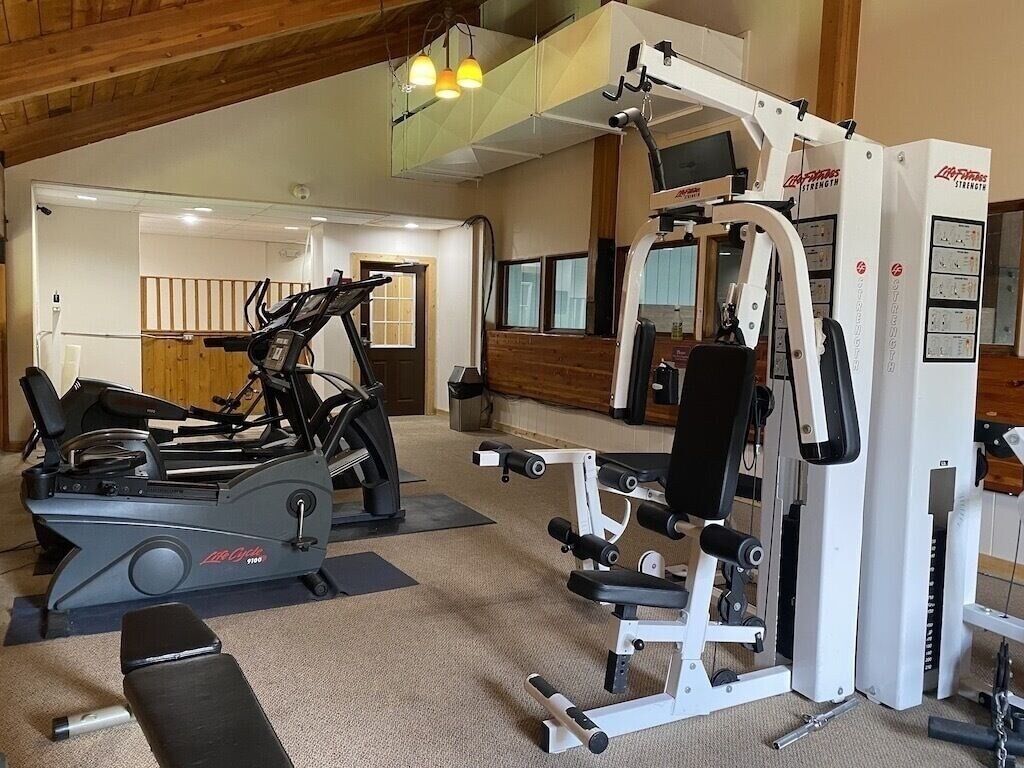 A gym with cardio machines, weightlifting equipment, and a bench.