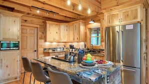 A wooden cabin-style kitchen with a granite countertop, stainless steel appliances, and a large island with bar stools.