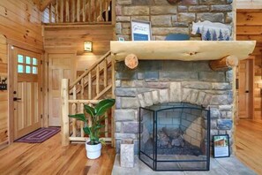 A stone fireplace with a wooden mantel, a potted plant, and a fireplace screen.