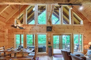 A log cabin interior with a dining area, large windows, and a ceiling with elk antlers.