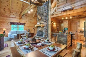 L’intérieur d’une cabane en rondins, avec une cheminée en pierre, une table à manger en bois et un coin cuisine.