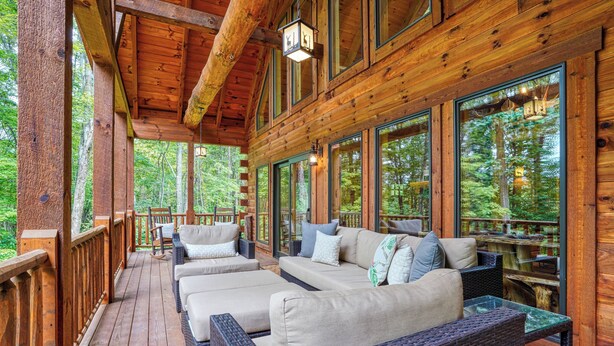 A wooden deck with wicker furniture and large windows overlooking a forest.