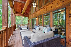 Une terrasse en bois, meublée de meubles en osier, avec de grandes fenêtres donnant sur une forêt.