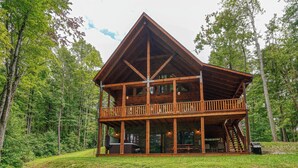 A two-story log cabin with a balcony, surrounded by a forest.