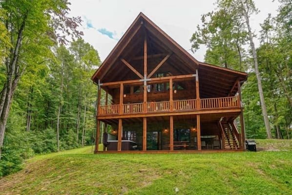A two-story log cabin with a balcony, surrounded by a forested area. - Bear Pines charming 3 bdrm cabin, Hot Tub, WiFi, in scenic South Bloomingville (South Bloomingville)