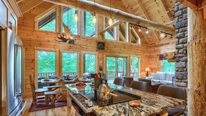 A log cabin with a large kitchen area featuring a granite countertop, wooden dining table, and a stone fireplace.
