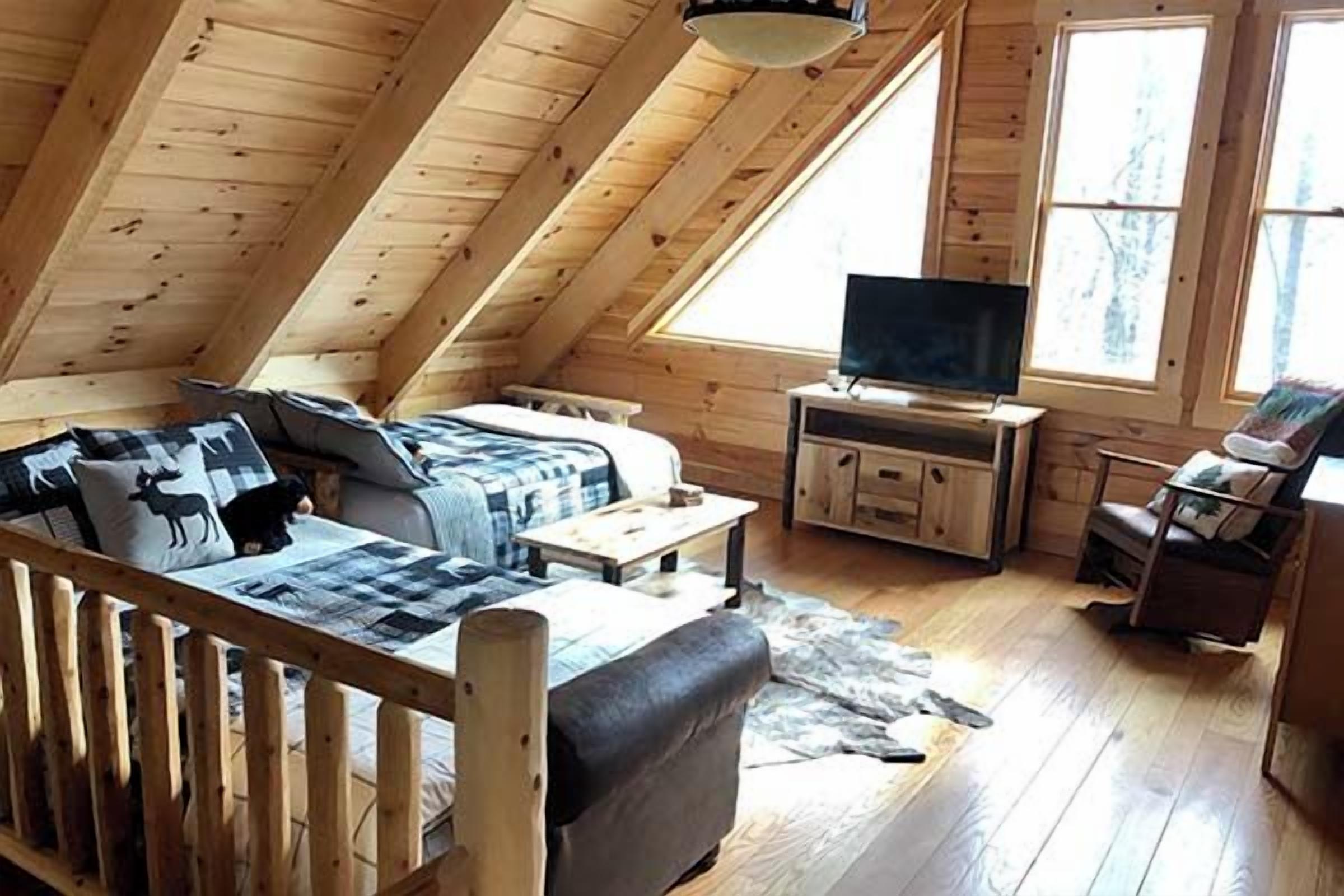 A cozy loft-style room with a wooden ceiling, a sofa, a television, and a chair.