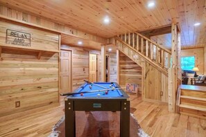 Un interior de madera con mesa de billar, una escalera y un televisor.