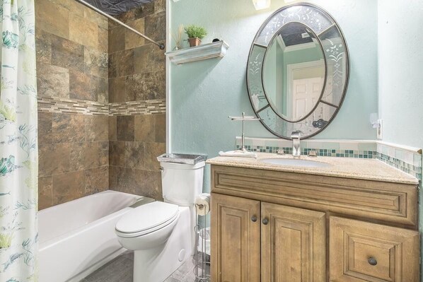 A bathroom with a bathtub, toilet, vanity with a mirror, and a shower area. - Blue Surf 17B (Miramar Beach)