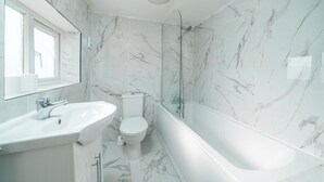 A modern bathroom with a marble floor, a glass-enclosed shower, a white sink, and a toilet.