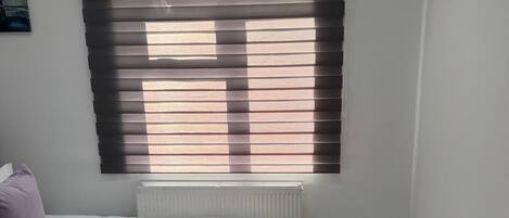 A small, clean room with two beds, a radiator, and a window with blinds.