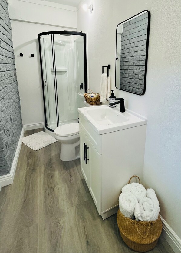 A modern bathroom with a glass shower enclosure, a white sink, and a mirror with a brick pattern. - Private suite with own entry in vibrant Gainesville (Gainesville)