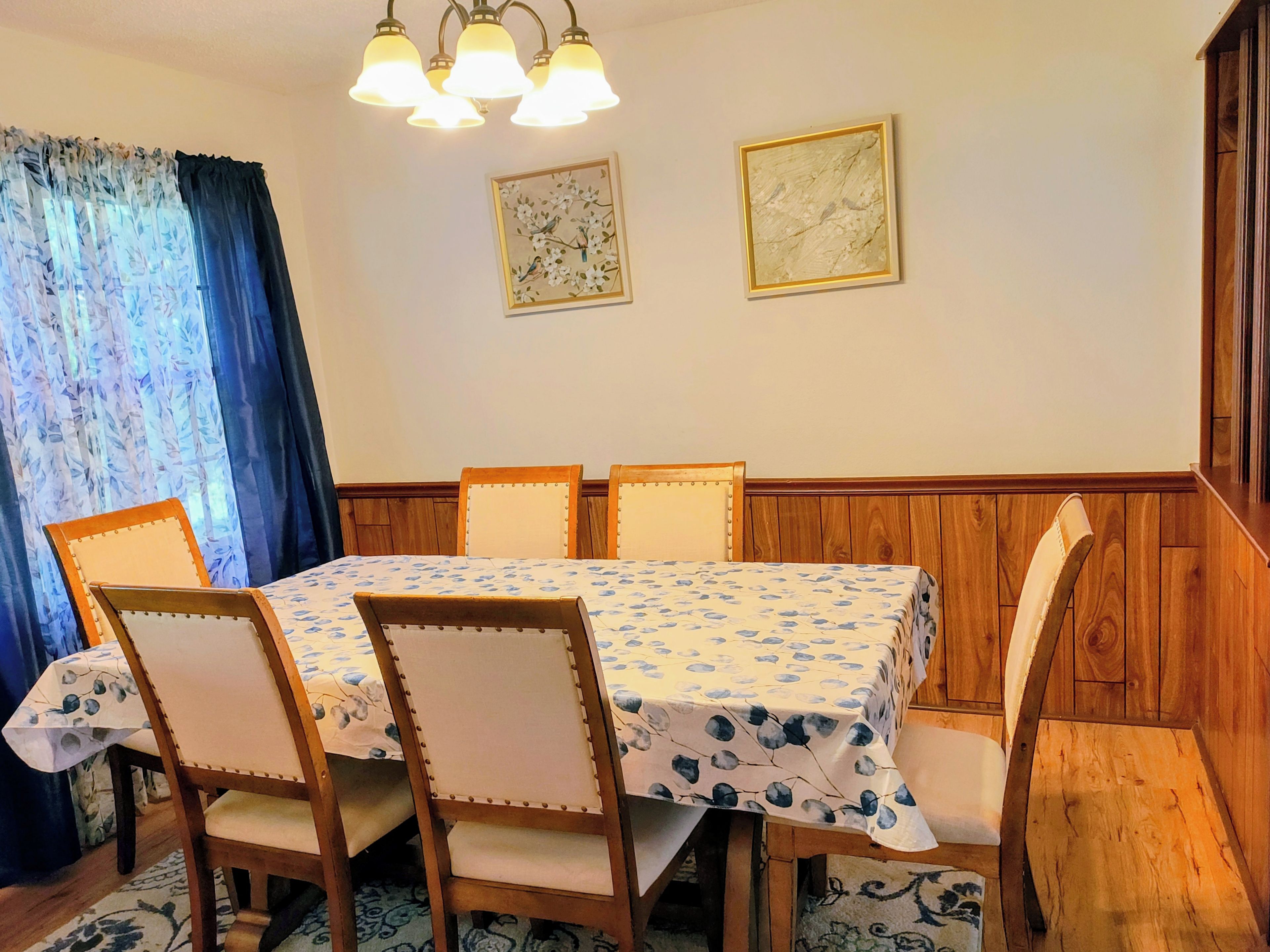 A dining area with a wooden table and chairs, a chandelier, and two framed pictures on the wall.