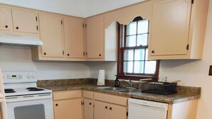 Una cocina con armarios de madera, una estufa blanca, un lavavajillas y una ventana.