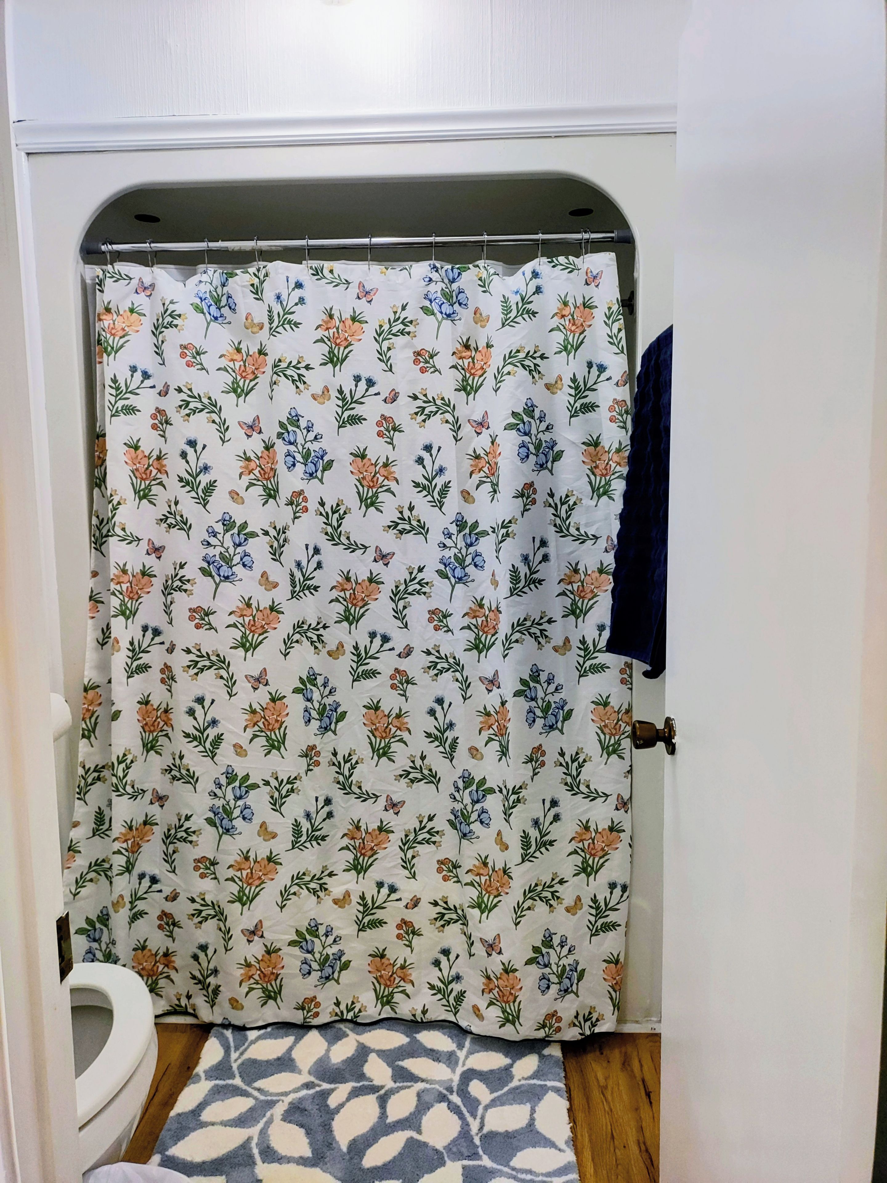A bathroom with a shower curtain featuring a floral pattern, a white toilet, and a patterned rug on the floor.