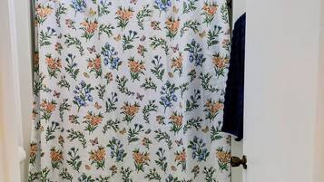 A bathroom with a shower curtain featuring a floral pattern, a white toilet, and a patterned rug on the floor.