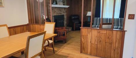 Ein Holzespeisesaal mit Stühlen, ein Kamin, ein Fernseher und ein gestreiftes Sofa in einem Raum mit Holzwänden und einem Deckenventilator.