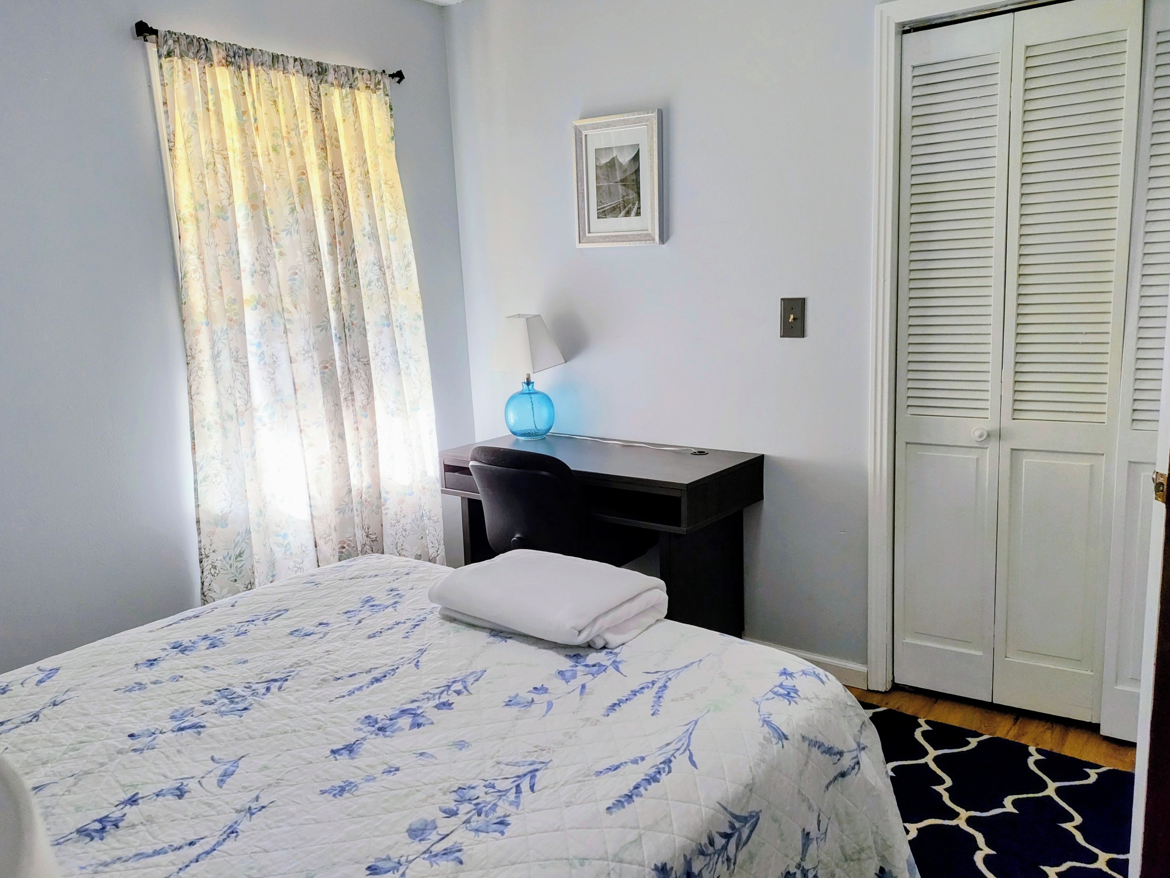 Una camera da letto con un letto, una scrivania, una sedia, una lampada e un armadio.