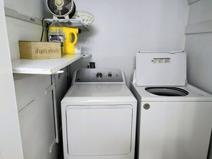 A compact laundry area with a front-loading washer and dryer, a shelf with a box labeled 'dryer sheets,' and a bottle of 'Olde Time' dishwashing liquid. - 3-bedroom house in awesome Corinth with WiFi, AC. No cleaning fees (Corinth)