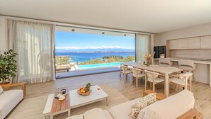Een moderne woonkamer met een groot raam met uitzicht op een zwembad en de zee.
