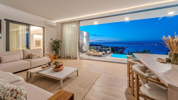 Een moderne woonkamer met een bank, salontafel en een eethoek met uitzicht op zee.