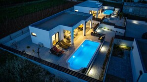 Une maison moderne dotée d’une piscine, d’un espace salon extérieur et d’une terrasse bien éclairée.