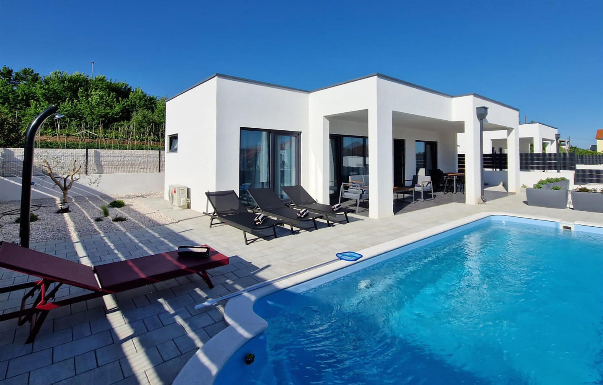 Uma área moderna junto à piscina com uma piscina azul cristalina, espreguiçadeiras e um espaço coberto para relaxar.