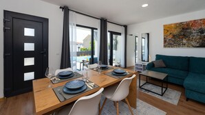 Un coin repas moderne avec une table en bois dressée pour quatre personnes, des chaises blanches et un canapé turquoise en arrière-plan.