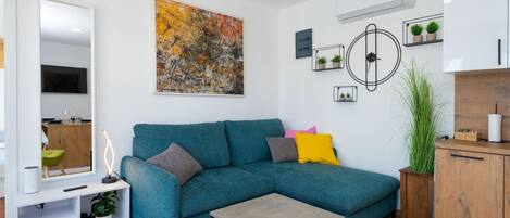 Uma sala de estar moderna com um sofá verde-água, uma mesa de centro, um quadro abstrato grande, um ar condicionado fixado na parede e um armário de madeira.