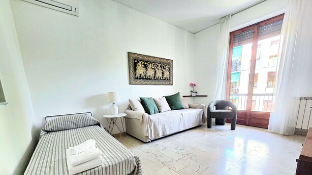 A hotel room with a bed, a sofa, a chair, a small table with a lamp, and a decorative wall piece. - Michelle apartment with private parking (La Spezia)