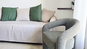 A living room with a sofa, green and beige cushions, a decorative wall hanging, and a unique chair. - Michelle apartment with private parking (La Spezia)