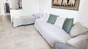 A modern, minimalist bedroom with a large bed, a sofa, and a small armchair. There is a wall-mounted artwork depicting a historical scene. - Michelle apartment with private parking (La Spezia)