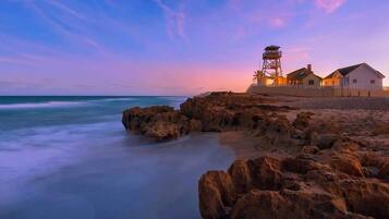 A coastal hotel with a lighthouse, beach, and rocky shoreline.