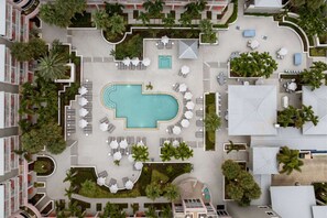 An aerial view of a hotel with a central swimming pool, multiple lounge areas with umbrellas, and surrounding greenery. - Near Ocean Club Golf | 2 King Room & Balcony (Stuart)