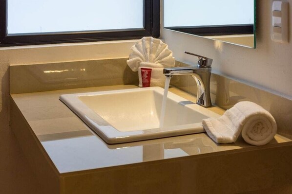 A bathroom sink with a white basin, a silver faucet, and a rolled white towel on the counter.