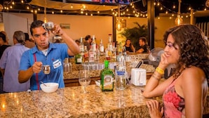 A bar area with a granite countertop, bottles of liquor, glasses, and a fan. - Hostel Boutique & Beach Club Agua y Fuego - Adults Only (Cancun)