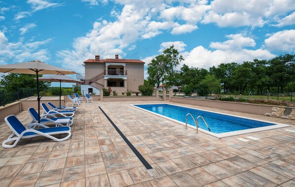 A pool area with lounge chairs, a swimming pool, and a building with a balcony.
