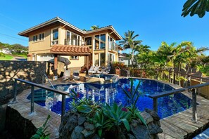 Une maison à deux étages dotée d’une piscine, d’un espace salon extérieur et d’un aménagement paysager de style tropical.