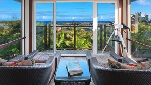 Un balcone con mobili in vimini, un telescopio e vista sull'oceano.